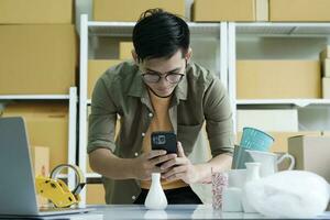 Young male online business owner using cellphone checking parcel box. photo