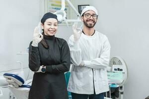 Portrait of dentist and her assistant in the office, female dentist and her assistant thumbs up, oral professionals portrait photo