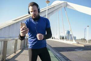 A closeup shot of a male in blue headphones using his mobile while jogging in the street photo