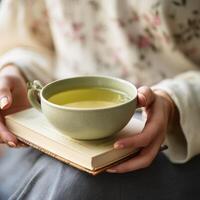 Calm scene of hands cradling a green tea cup with a mindfulness book nearby photo