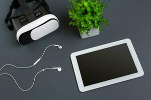 Virtual reality glasses and tablet with headphones on a gray background. Top view photo