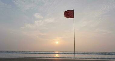 red flag on beach on sea or ocean at sunset as symbol of danger. The sea state is considered dangerous and swimming is prohibited. video