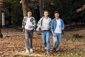 Three teenage boys, posing in nature, rejoicing, running and having fun. Teenage classmates are resting against the background of an autumn forest. photo