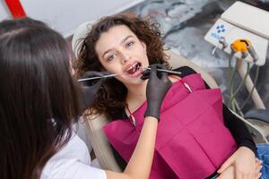 Closeup of female patient showing her beautiful white teeth while having treatment at dental clinic, dentist hands in rubber gloves holding dental tools photo