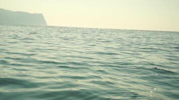 Sea water surface. Camera flies over the calm azure sea with volcanic rocky shores on background. Nobody. Holiday recreation concept. Abstract nautical summer ocean nature. Slow motion. Close up video