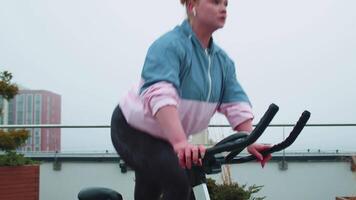 Athletic woman riding on spinning stationary bike training routine on house rooftop, weight loss video