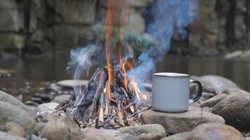 uma caneca em uma pedra perto uma fogo em a rio banco, fechar-se. viagem conceito. 4k video