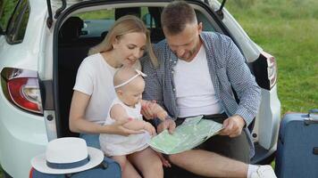 feliz família viajando de carro. uma pai e mãe aguarde uma bebê menina dentro seus braços e Veja às uma estrada mapa. ativo lazer para a família video