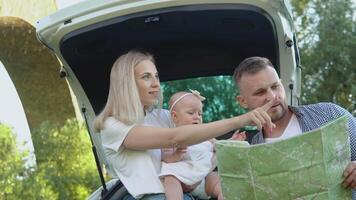 feliz família viajando de carro. uma pai e mãe aguarde uma bebê menina dentro seus braços e Veja às uma estrada mapa. ativo lazer para a família video