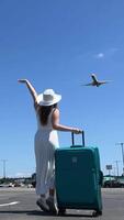 uma jovem lindo menina dentro uma branco vestir e uma chapéu com uma mala de viagem ondas dela mão para uma vôo avião viagem período de férias alegria saltar ter Diversão senhorita a avião pressa para sair uma Novo chance dentro vida video