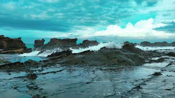 aerial top view of waves break on rocks in a blue ocean. sea waves on beautiful beach aerial view drone. bird's eye view of ocean waves crashing against an empty stone rock cliff from above video