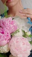 Young woman receives bouquet of flowers. Happy girl holding bouquet of peonies. Female presses a bouquet of pink peonies to her chest and sniffing flowers, slow motion. International Women Day video