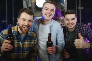 Young men in casual clothes are talking, laughing and drinking while sitting at bar counter in pub photo