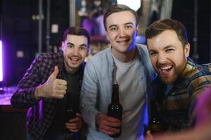 Friends having fun. Happy young men in casual wear drinking beer in pub. photo