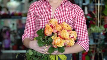 Woman florist standing and holding bouquet of roses in flower shop, close up video