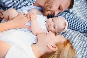 mamá, papá y pequeño hijo acostado en el cobija en el verano parque. el concepto de verano día festivo. de madre, del padre, del bebe día. familia gasto hora juntos en naturaleza. familia Mira foto