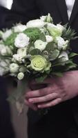 Handsome businessman holding flowers. Groom in a suit holding a bouquet of flowers. Wedding boutonniere. Elegant man dressed in a modern black suit and white shirt holding in hand a wedding flowers video