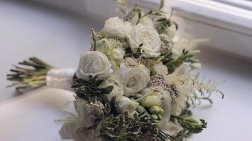 Wedding golden rings lie on beautiful wedding white rose flowers bouquet on white window sill video