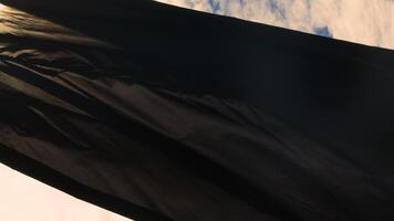 black flag without an emblem flutters against the blue sky with sun reflections. video