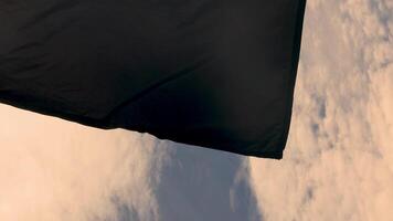 black flag without an emblem flutters against the blue sky with sun reflections. video