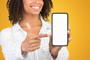 Modern Technology Concept. African american woman pointing at blank phone screen, mock up photo