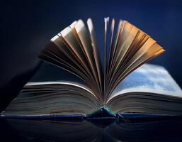 An open book with fanned pages displayed against a dark background, capturing a dramatic and reflective light effect. photo