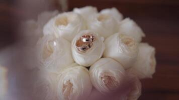 Wedding golden rings lie on beautiful wedding white rose flowers bouquet on the brown tablet video