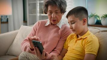 Caucasian grandmother grandson enjoying time together on couch home old woman grandma kid boy grandchild using mobile phone shopping in online store teaching learning modern technology on smartphone photo