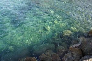 Clear, turquoise water laps against the rocks on a sunny day photo