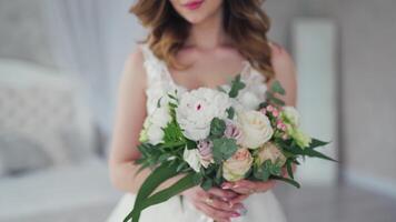 Wedding bouquet of creamy roses in the hands of a beautiful bride. Lovely young woman dressed in white wedding dress is holding flowers. Close-up. video