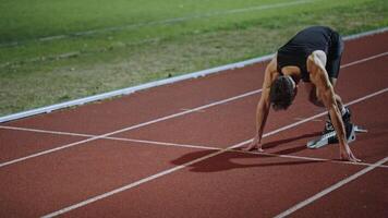 Strong Young Man Starting a Race From Track Starting Blocks Position on a Dark Stadium in the Evening. Cinematic Portrait of a Fit Male Sprint Runner Participating in a Competition video