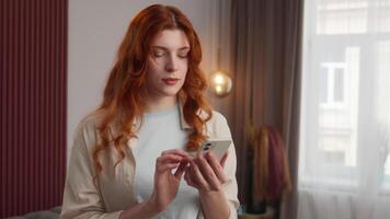 Caucasian woman female hold mobile phone scrolling touch smartphone screen redhead girl checking sms shocking news omg reaction fear emotion at home surprise afraid lady open mouth revelation anxiety video