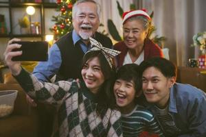 família asiática tomando selfie perto da árvore de natal juntos em casa. família, férias, conceito de natal foto