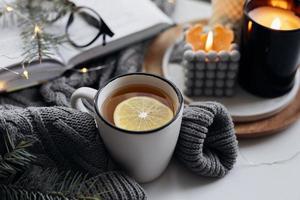 conceito aconchegante de casa de inverno. caneca com chá de limão, livro aberto, suéter quente, velas e abeto. bem-estar, conceito relaxante foto