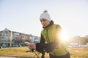 Frau mit Smartphone während gelehnt auf ein Fahrrad foto