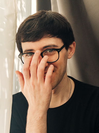 Photo portrait of Matthew, smiling at the reader as he adjusts his glasses.