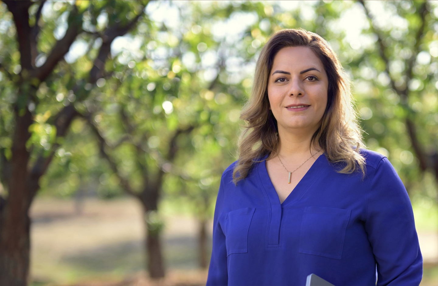 Desireh, ayakta durarak kolunun altında bir MacBook ile kameraya doğru gülümsüyor