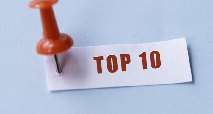 Small white paper pinned with a red pin on blue background. Top 10 is written on the paper .