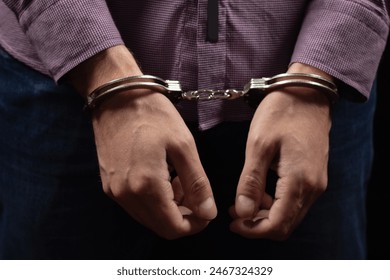 Businessman in handcuffs arrested for financial fraud, sitting in interrogation room.