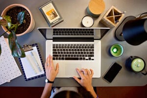 Overhead shot of person typing at a laptop with study materials surrounding.