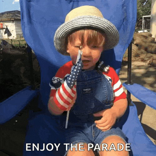 a little boy in overalls and a hat is sitting in a blue chair holding an american flag and the words enjoy the parade below him