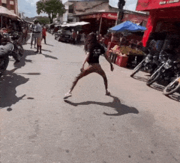 a woman is dancing on the street in front of a row of motorcycles parked on the side of the road .