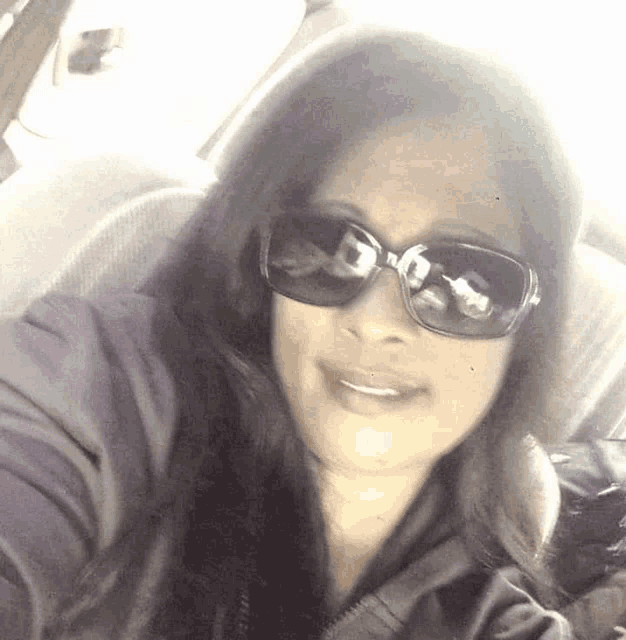 a woman wearing sunglasses is sitting in a car and smiling