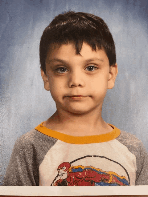 a young boy wearing a shirt with a superhero on it poses for a picture