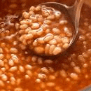 a close up of a spoon in a pot of soup with beans .