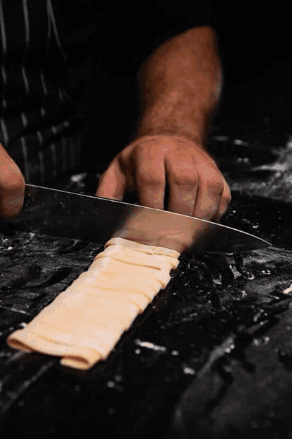 a person is cutting a piece of pasta with a large knife