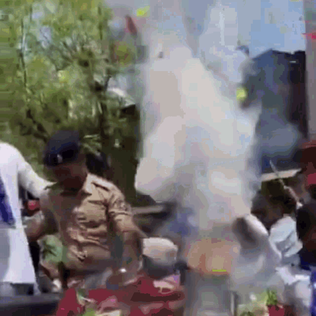 a police officer is standing in front of a crowd of people with smoke coming out of a building .