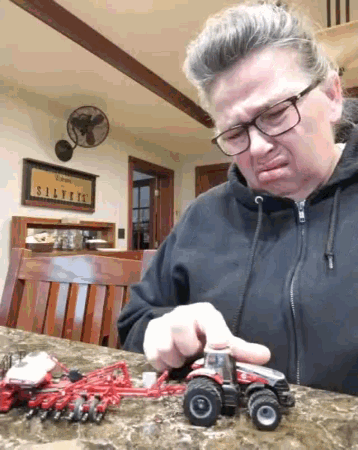 a woman wearing glasses is playing with a toy tractor on a table in front of a sign that says silvers