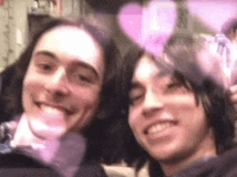 two young men are posing for a picture together with pink hearts behind them .