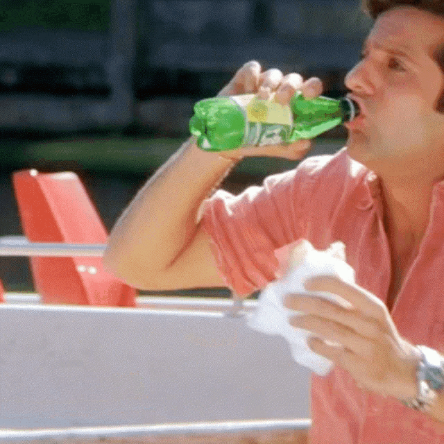 a man in a pink shirt is drinking a bottle of sprite